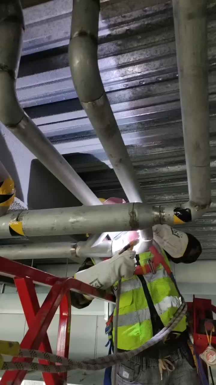 Worker in gloves and high-visibility workwear welding overhead pipework