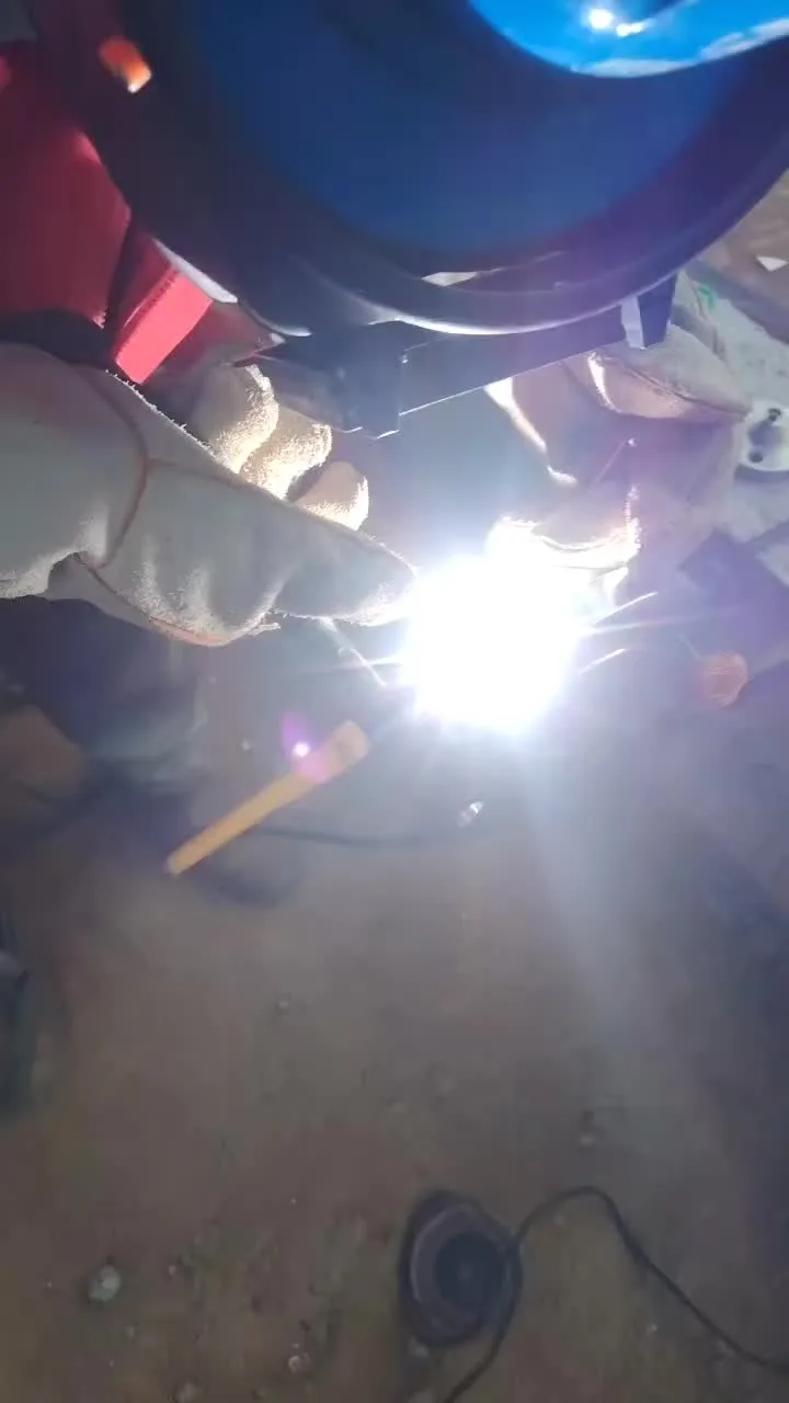A welder grinding a steel pipe on the shop floor — properly fitted gloves let the hands move freely during heavy work