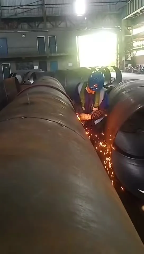 Welder in protective gloves working on large pipes as sparks fly in a fabrication shop