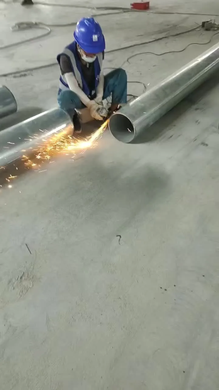 A welder grinding a steel pipe on the shop floor — properly fitted gloves let the hands move freely through grinding, fitting, and welding.